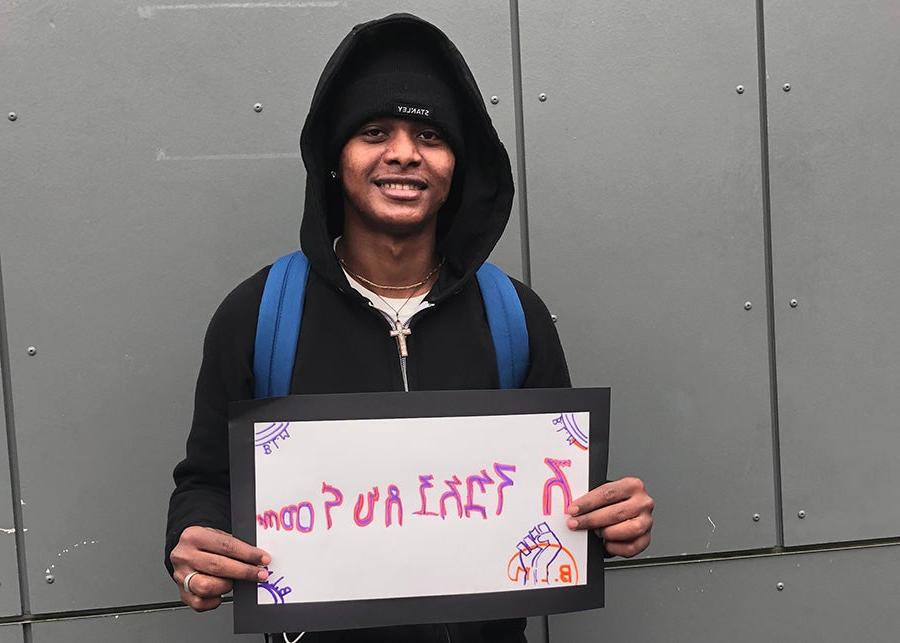 A student smiles for a photo with a sign that says welcome in Amharic